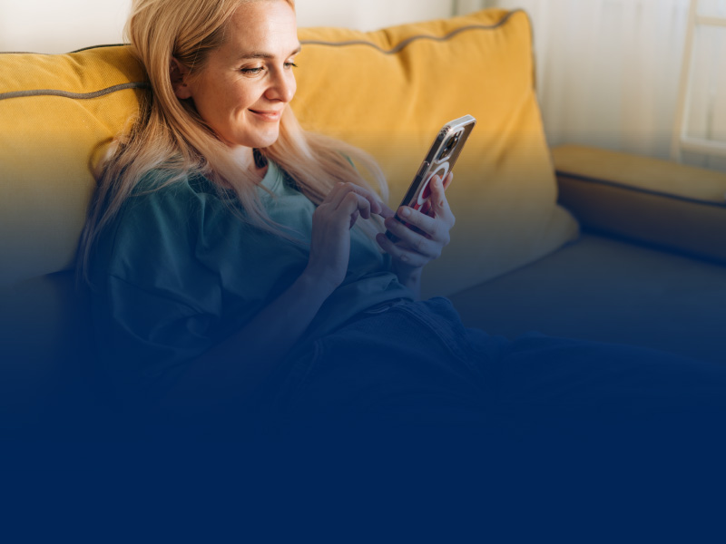 Frau liegt auf dem Sofa und liest am Smartphone