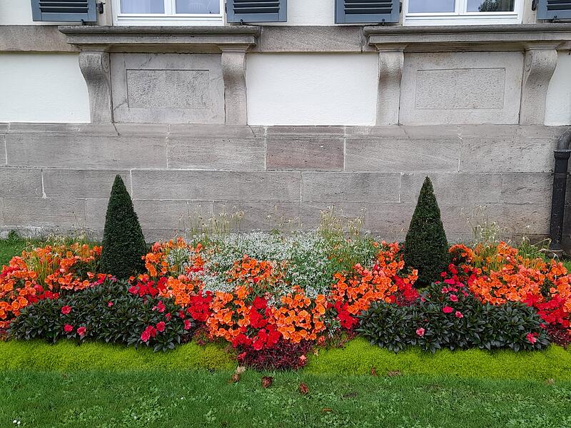 Wer sich im Bad Brückenauer Staatbad im Schlosspark dem Elisabethenhof nähert, erfreut sich rechts und links vom Haupteingang an leuchtenden Teppichbeeten. Ganz dicht sind die orangen, roten und weißen Sommerpflanzen nebeneinander gesetzt, sodass man den Eindruck eines Teppichs hat.