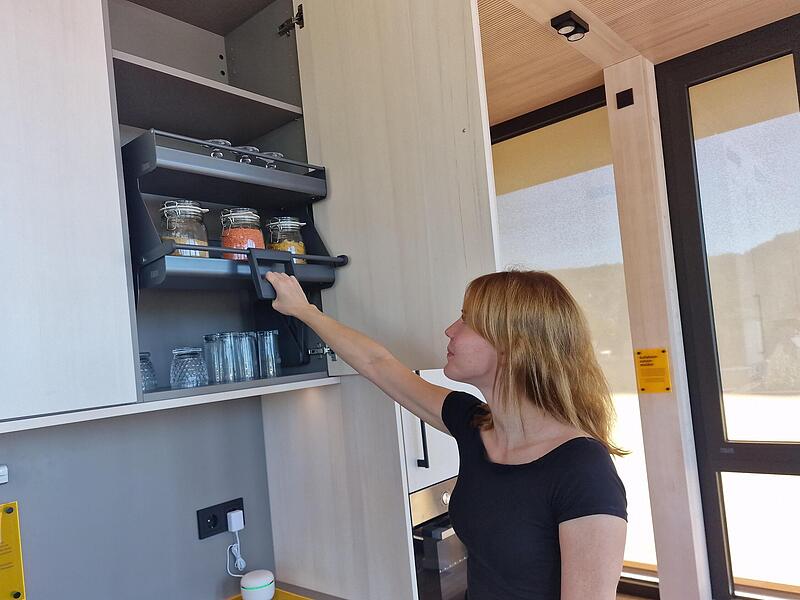 Stefanie Tratt demonstriert, wie ein absenkbarer Oberschrank auch hohe Bereiche in der  K&uuml;che erreichbar  macht.