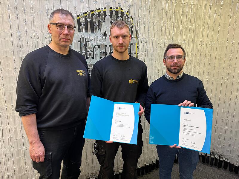 Ausbilder Andreas Perkowski (von links), Absolvent Lukas Fiedler und Ausbildungsmanager Dominik K&uuml;nzel halten die Urkunden f&uuml;r den Geehrten und Heinz-Glas in den H&auml;nden.