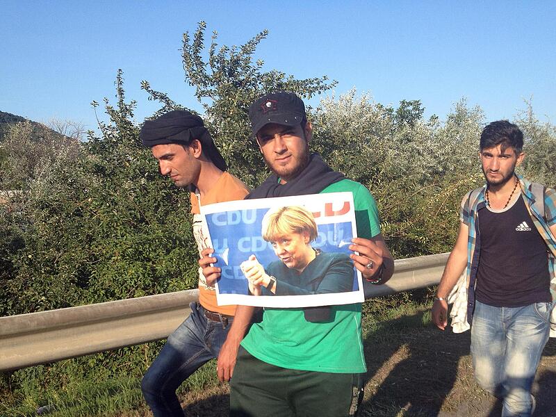 Mit einem Foto von Bundeskanzlerin Merkel gehen syrische Flüchtlinge in der Nähe von Budapest eine Straße in Richtung österreichische Grenze entlang. Am 4. September 2015 machten sich Hunderte Flüchtlinge in Ungarn auf Richtung Deutschland.
