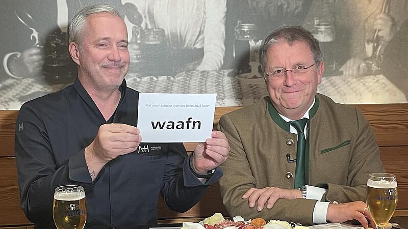 Nach „„Erpfl“ im vorigen Jahr wurde das Wort „waafn“ zum oberfränkischen Wort des Jahres 2022 gekürt. Bezirkstagspräsident Henry Schramm (rechts) gab das Wort gemeinsam mit dem oberfränkischen Starkoch Alexander Herrmann (links) bekannt.