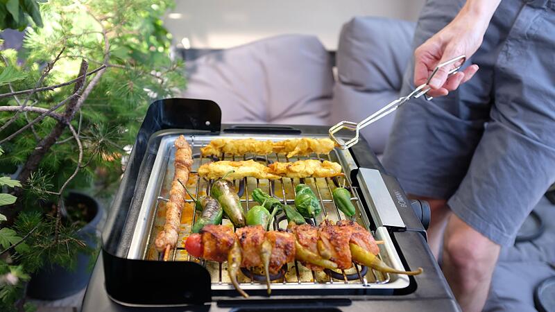 Ein Mann grillt mit einem Elektrogrill auf einem Balkon