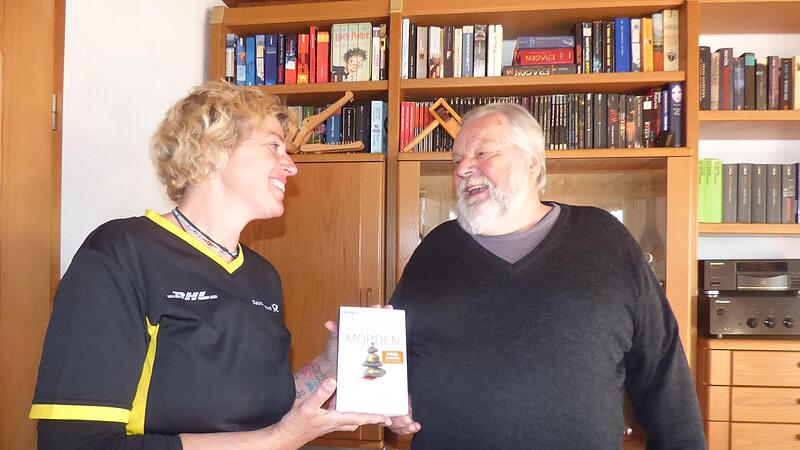 Postbotin Carola Gath &uuml;bergibt Ingo Klinger in dessen Wohnzimmer ein Buch.Forchheim & Fr&auml;nkische Schweiz