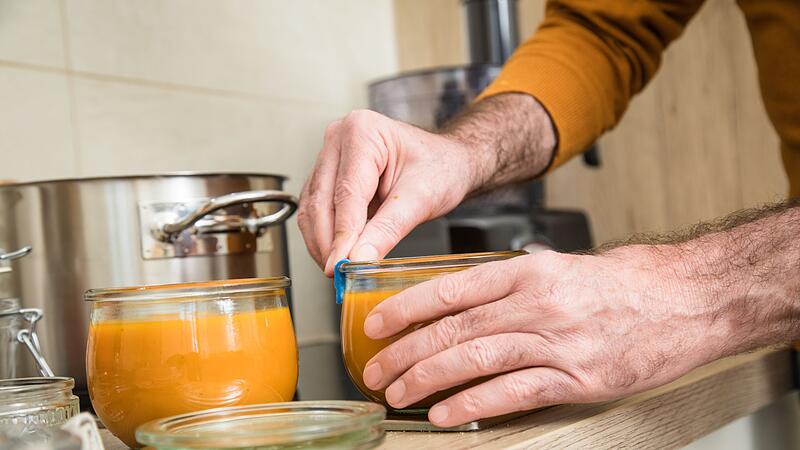 Ein Mann füllt Kürbismuß in Einweckgläser
