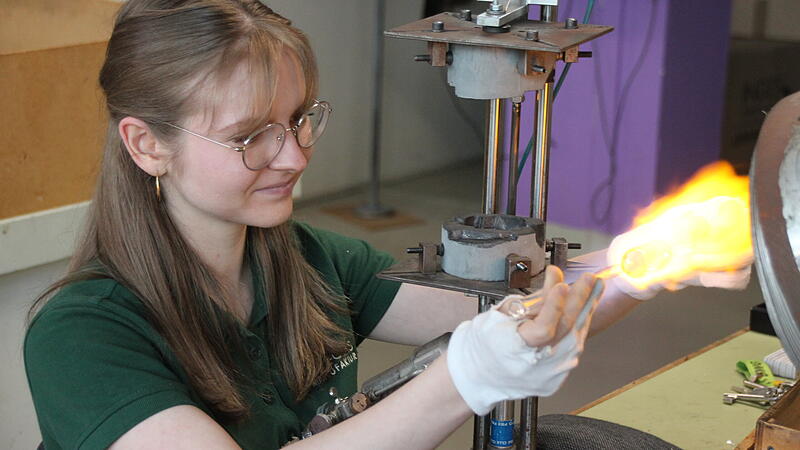 Olesja Pilipeev bereitet den Glaskolben vor, damit er in der Form geblasen werden kann.