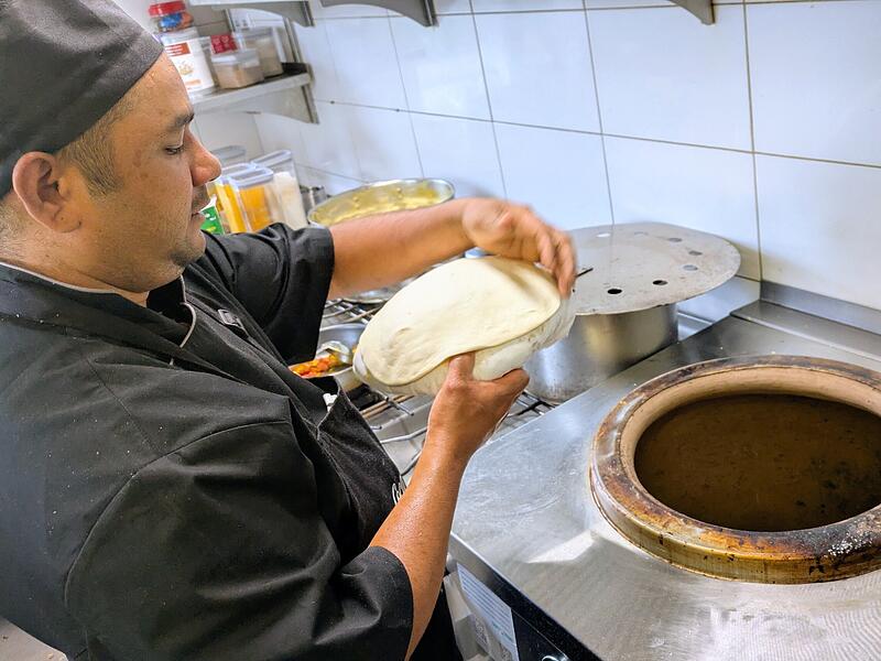 Koch Rajesh Rawat beim Backen des indischen Naan-Fladenbrotes am typischen Tandoor-Lehmofen