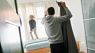 Mann bezieht ein Bett während ein Kind auf dem Bett hüpft Mann bezieht ein Bett während ein Kind auf dem Bett hüpft