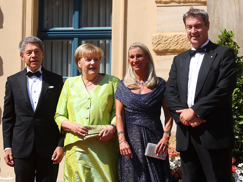 Angela Merkel (2.vl), ehemalige Bundeskanzlerin, und Ehemann Joachim Sauer (l) stehen mit Markus S&ouml;der, Ministerpr&auml;sident Bayerns, und seiner Frau Karin zusammen vor der Er&ouml;ffnung der Bayreuther Richard-Wagner-Festspiele im Festspielhaus auf dem Gr&uuml;nen H&uuml;gel.