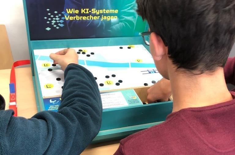 Wie helfen KI-Systeme der Polizei bei der Verbrecherjagd? Um diese Frage dreht sich eine der Stationen des Lernlabors „Künstliche Intelligenz aus der Kiste.“ Wie helfen KI-Systeme der Polizei bei der Verbrecherjagd? Um diese Frage dreht sich eine der Stationen des Lernlabors „Künstliche Intelligenz aus der Kiste.“