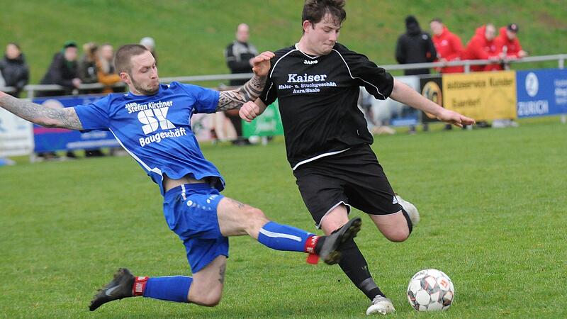Sandbergs Patrick Zehe (links) setzt hier noch in der ersten H&auml;lfte zur Gr&auml;tsche gegen Jannik Schmitt vom SV Aura an. Dann setzte der Dauerregen ein und der Unparteiische unterband diesen K&ouml;rpereinsatz vehement. Der SVA gewann knapp mit 3:2.