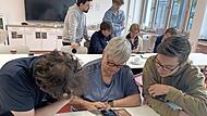 Zwei Schüler unterstützen eine Seniorin bei der Einstellung der Standortfreigabe auf ihrem Smartphone. Zwei Schüler unterstützen eine Seniorin bei der Einstellung der Standortfreigabe auf ihrem Smartphone.
