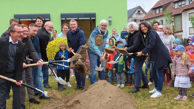 Schnell die kurze Regenpause zum Spatenstich genutzt: Am Sandberg von rechts) die Leiterin der Kita, die Architektin, der Bürgermeister, Vertreter des Elternbeirats und des Kirchenrats sowie Pfarrer Walter Ries (ganz li.) greifen zum Spaten.