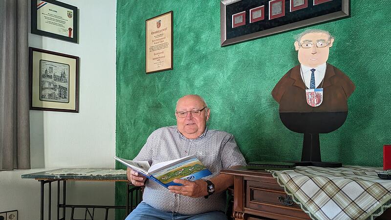 Sigfried Erhard in seinem Wohnzimmer: Neben ihm er selbst, ein Geschenk seiner Schule aus der Zeit als B&uuml;rgermeister. Dahinter eingerahmt Teile der B&uuml;rgermeisterkette, die Ehrenb&uuml;rgerurkunde der Gemeinde Oerlenbach und daneben die von Douvres, der Partnergemeinde Oerlenbachs.