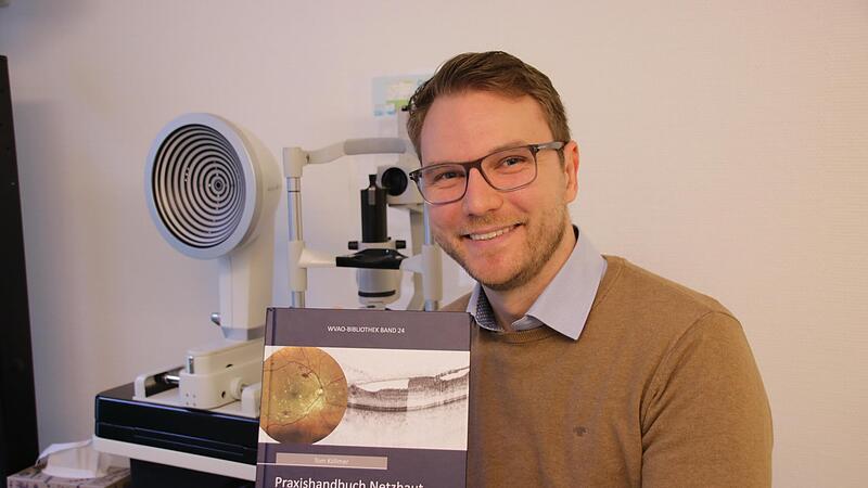 Tom K&ouml;llmer im heimischen Optikerbetrieb in der Grabengasse mit seinem Fachbuch zu Netzhauterkrankungen.