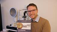 Tom K&ouml;llmer im heimischen Optikerbetrieb in der Grabengasse mit seinem Fachbuch zu Netzhauterkrankungen.