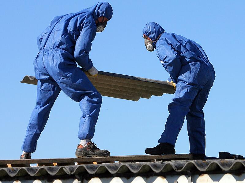 Arbeiter in Schutzkleidung demontieren Asbestplatten auf Dach