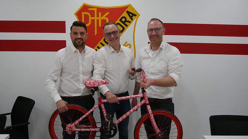 Mit einem speziellen DJK-Bike und einem Gutschein f&uuml;r eine neue Radler-Ausr&uuml;stung bedankten sich der 1. Vorsitzende Michael Schr&ouml;ter (links) und der 2. Vorsitzende Marcel Zimmermann (rechts) bei Frank B&uuml;cher, der 22 Jahre lang als engagierter Beis...