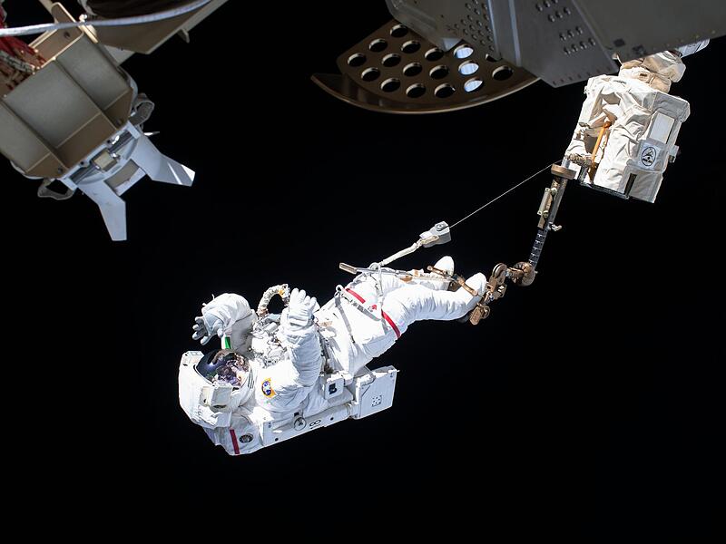 Ein ESA-Astronaut ist bei einem Au&szlig;eneinsatz an der Internationalen Raumstation ISS &uuml;ber den Roboterarm Canadarm2 gesichert. Bayern entwickelt sich  zu einem der wichtigsten Raumfahrt-Standorte in Europa.