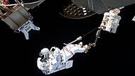 Ein ESA-Astronaut ist bei einem Au&szlig;eneinsatz an der Internationalen Raumstation ISS &uuml;ber den Roboterarm Canadarm2 gesichert. Bayern entwickelt sich  zu einem der wichtigsten Raumfahrt-Standorte in Europa.