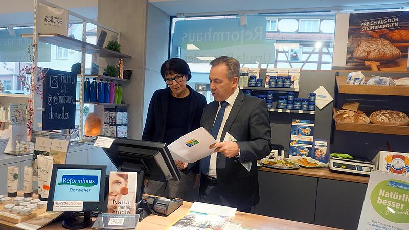 Ursula Dorweiler, Inhaberin des Reformhauses Dorweiler, und Landrat Alexander Tritthart blicken in die Urkunde des Umwelt- und Klimapakts Bayern. Der Betrieb in Herzogenaurach erh&auml;lt eine Auszeichnung f&uuml;r seine M&uuml;hen um den Klimaschutz.