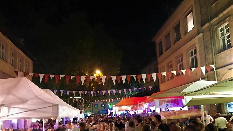 Sandkerwa-Streit eskaliert: Drei Verletzte, drei Personen in Gewahrsam Nachtfest mit Menschenmenge bei der Bamberger Sandkerwa. Bunte Wimpelketten schmücken die Straße, beleuchtete Stände und Zelte sind zu sehen. Lebhafte Atmosphäre bei einer Feier.