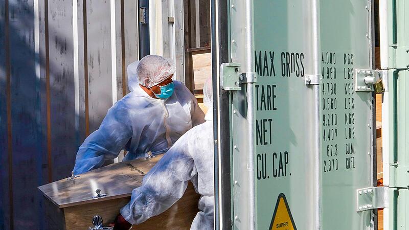 Bestattungsarbeiter   im s&uuml;dafrikanischen Kapstadt schieben  einen Sarg   mit einem Corona-Toten in einen K&uuml;hlcontainer.