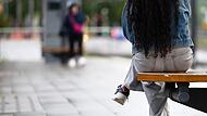 Eine junge Frau sitzt an einer Haltestelle auf einer Bank