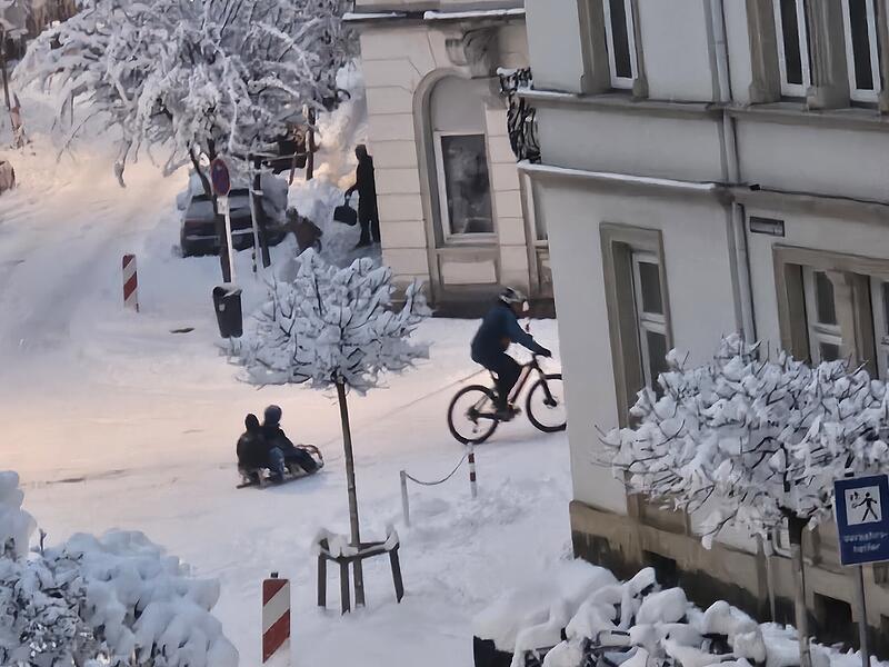 Schneevergn&uuml;gen in der Stadt. Ein Vater, wie er am gestrigen Abend (26.01.2026) mit seinem Fahrrad einen Schlitten mit seinen Kindern &uuml;ber die verschneite Stra&szlig;e zieht.