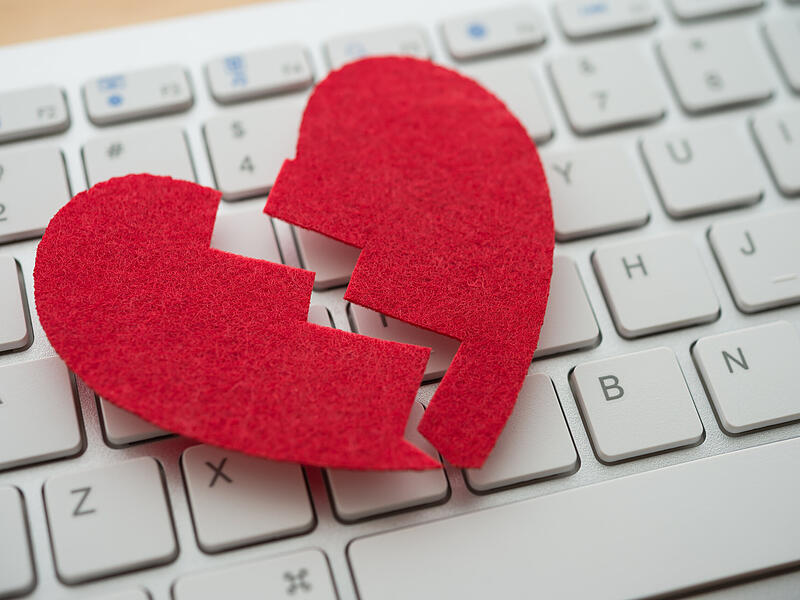 Red broken heart on white keyboard computer background. Online internet romance scam or swindler in website application dating concept. Love is bait or victim.