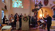 Heinrich Arnold (rechts) dirigiert den Kirchenchor „Klangvoll“. Die Gottesdienste werden live gestreamt, deshalb werden die Liedtexte für alle zum Mitsingen an die Wand projiziert. Seitdem, sagt Arnold verschmitzt, klinge auch der Gesang in der Ki...