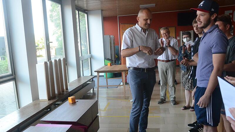 Rainer Dressler (links) &uuml;berreicht den Siegerpreis an Jannik Himmel (rechts). Links am Boden steht das vom angehenden Schreinergesellen kreierte und angefertigte Gesellenst&uuml;ck, ein extravagantes Sideboard.