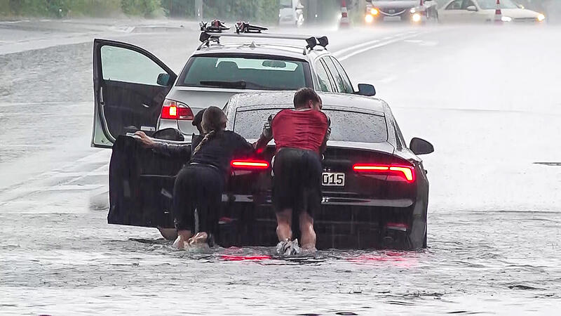 Trotz Warnung fuhren mehrere Autofahrer durch die &uuml;berfluteten Unterf&uuml;hrungen. Hier versuchen zwei Menschen, ein Fahrzeug auf dem M&uuml;nchner Ring zu retten.