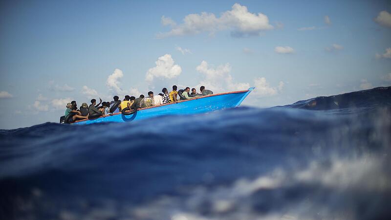 Migranten sitzen in einem Holzboot s&uuml;dlich der italienischen Insel Lampedusa auf dem Mittelmeer. Die Zahl der Asylantr&auml;ge in der EU steigt &ndash; was zu Debatten &uuml;ber die Verteilung sorgt.