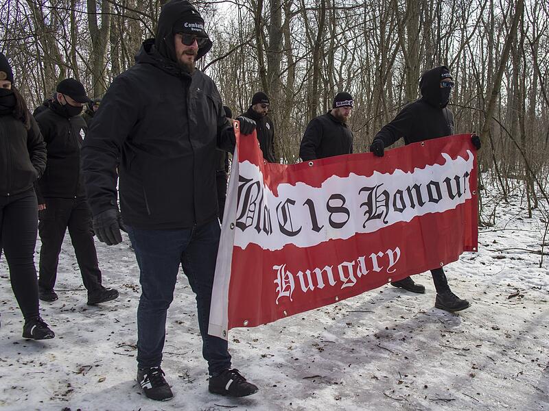 Diese Neonazis marschierten ebenfalls beim "Tag der Ehre" in Budapest am 11. Februar 2023 auf. Auf ihrer Fahne steht "Blood" (Blut), "Honour" (Ehre) und "Combat 18". Die Zahlen eins und acht stehen im Alphabet für A und H. Somit kann übersetzt werden, dass hier die "Kampfgruppe Adolf Hitler" unterwegs war.  Deren Mitglieder trafen sich auf dem Normafa-hügel, um von dort hinunter zur Budaer Burg zu wandern.