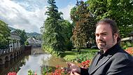 Thorsten Schlotter spielt in diesem Jahr beim Rakoczy-Fest erstmals die Rolle des F&uuml;rtsbischofs Friedrich Carl Graf von Sch&ouml;nborn. F&uuml;r unser Foto posiert er an der Saale, die der historische Sch&ouml;nborn 1737 am heutigen Kurgarten verlegen lie&szlig;, wobei die Rakoczy-Quelle wiederentdeckt wurde.  Ein schweres Kreuz und ein Ring mit Edelstein geh&ouml;ren zum Kost&uuml;m des F&uuml;rstbischofs dazu.