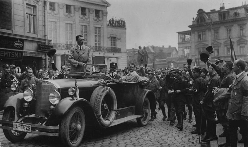 Adolf Hitler wird bei seiner Ankunft in Weimar von SA-M&auml;nnern begr&uuml;&szlig;t. Im Fond des Wagens Rudolf He&szlig; &ndash; Aufnahme vom 03./04.07.1926