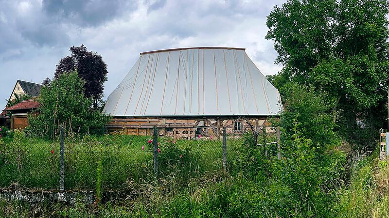 Nach Jahrzehnten des Verfalls wurde das historische Schwedenhaus in Poxdorf zun&auml;chst notgesichert. Die schweren Dachziegel wurden vollst&auml;ndig abgenommen, um das gesch&auml;digte Tragwerk zu entlasten. Eine gro&szlig;fl&auml;chige Schutzfolie bewahrt das Geb&auml;ude vor weiterem Wassereintritt.