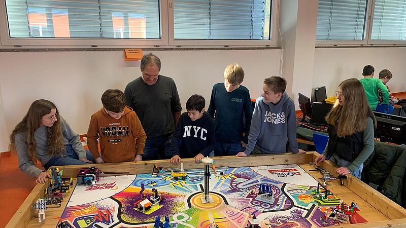 Lilli Rippstein, Moritz Beck, Coach Jürgen Hack, Florian Metz, Joel Löhnert, Marvin Eisenmann und Selina Cerny (von links) sitzen an ihrem Tisch, auf dem programmierte Roboter spezielle Aufgaben erfüllen müssen.