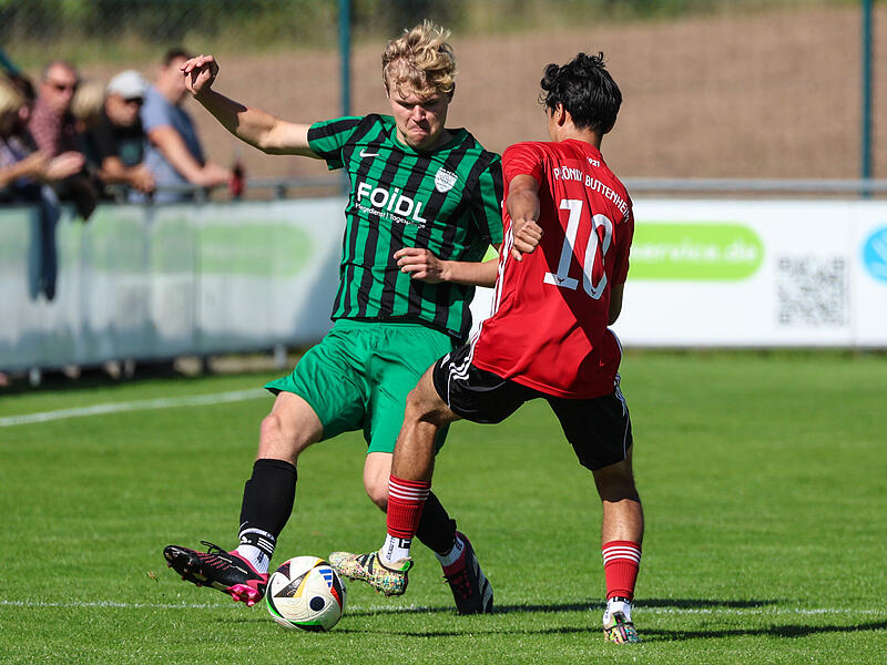 Neukenroths Julius Wagner (grün) hält gegen den Buttenheimer Jason Crittenton den Fuß vor und verhindert das Abspiel.