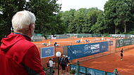 Aufschlag für das ITF German Juniors-Turnier in Bamberg. Mitorganisator und langjähriger Vereinsvorsitzender TC Bamberg – Axel Tschache – schaut auf die Plätze und beobachtet, wie sich Spielerinnen und Spieler aus über 40 Nationen zum Beginn des dritten Turniertages einspielen.