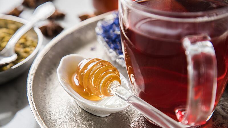 Ein Honiglöffel mit Waldhonig liegt neben einer Tasse Tee
