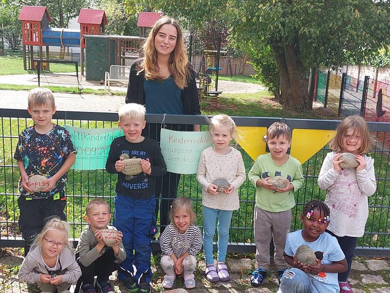 Die Kinder mit den Steinen, die zum Weltkindertag beschriftet wurden. Hinten: stv. Kindergartenleiterin Julia Schmitt.
