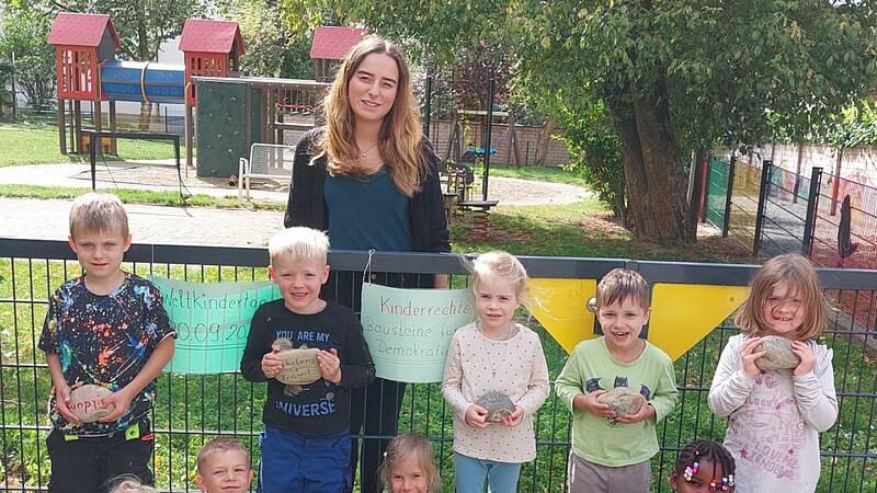 Die Kinder mit den Steinen, die zum Weltkindertag beschriftet wurden. Hinten: stv. Kindergartenleiterin Julia Schmitt.