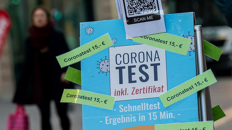Eine Frau geht in der Innenstadt an einem Schild mit der Aufschrift &bdquo;Corona Test - inkl. Zertifikat - Coronatest 15,- Euro&ldquo; vorbei, das vor einer Apotheke in der Innenstadt steht.