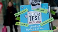 Eine Frau geht in der Innenstadt an einem Schild mit der Aufschrift &bdquo;Corona Test - inkl. Zertifikat - Coronatest 15,- Euro&ldquo; vorbei, das vor einer Apotheke in der Innenstadt steht.