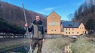 Daniel B&auml;rthlein steht mit einem Kescher an den Fischbecken und dem Bach vor der Thoosm&uuml;hle.