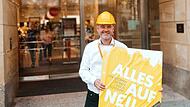"Alles auf neu": Mit diesem Schild in der Hand symbolisiert Filialgeschäftsführer Mathias Baluses mit gelbem Helm den Umbaustart der "Galeria" in Bamberg. An der Fassade steht - noch - "Karstadt".