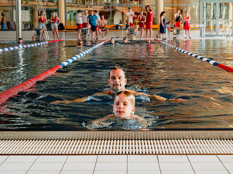 Konzentriert schwimmt der siebenj&auml;hrige Constantin Sack seine Bahn f&uuml;r das Deutsche Schwimmabzeichen in Bronze. Direkt hinter ihm folgt sein Vater Andr&eacute;. Im Hintergrund verfolgen weitere Teilnehmer und Pr&uuml;fer das Geschehen im Hallenbad des K&ouml;nigsbads in Forchheim.