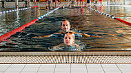 Konzentriert schwimmt der siebenj&auml;hrige Constantin Sack seine Bahn f&uuml;r das Deutsche Schwimmabzeichen in Bronze. Direkt hinter ihm folgt sein Vater Andr&eacute;. Im Hintergrund verfolgen weitere Teilnehmer und Pr&uuml;fer das Geschehen im Hallenbad des K&ouml;nigsbads in Forchheim.